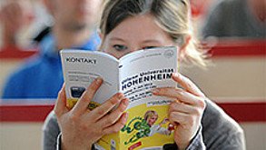 Eine Person liest eine Broschüre, auf deren Umschlag prominent die Texte „Kontakt“ und „Hohenheim“ stehen.